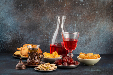 Ramadan kareem Iftar evening meal with dates, baklava, traditional Arabic sweets, fruit, Arab tea, rose sherbet beverage in glass jug. Islamic festive decorated dinner, Ramadan food composition 
