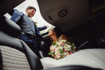 Beautiful wedding couple is riding in a luxury limousine with an open hatch.