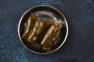 Traditional Middle Eastern dish Dolma in vine leaves in rustic metal plate on blue rustic background top view. Arab meze for snack or lunch, Middle Eastern cuisine 
