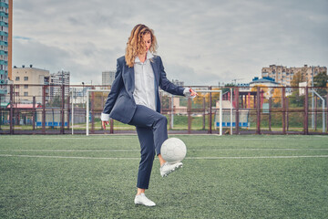 girl in an office suit hitting hitting soccer ball on the stadium field. concept
