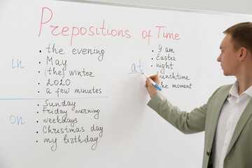 English teacher giving lesson on prepositions of time near whiteboard in classroom