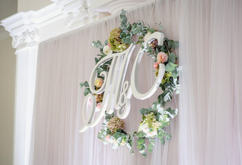 Green wreath decorated with flowers, letters hanging on a white background from fabric. The wooden...