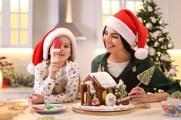 Mother and daughter having fun while decorating gingerbread house at table indoors