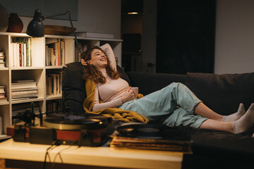 woman relaxing on sofa at her home, she is listening to a music on record player