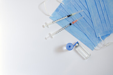 Creative ideas of vaccination concept. Top view of syringe with medical masks and vaccine vial glass bottles for vaccination against COVID-19. Coronavirus pandemic. Copy space. 