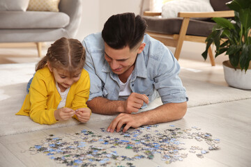 Happy father and his daughter playing with puzzles on floor at home