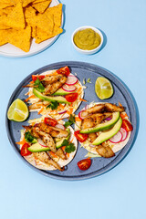 Tacos with crispy fish, avocado, guacamole sauce, nachos chips and lime on blue background. Top view. Mexican cuisine - 427885817