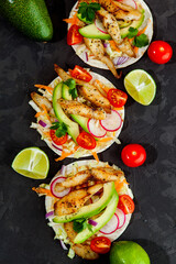 Tacos with crispy fish, avocado, guacamole sauce and lime on dark background. Top view. Mexican cuisine - 427885871
