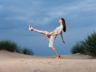 A woman in a beige dress walks with a long stride on the beach