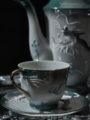 A retro luxurious porcelain cup of tea and a teapot against a black background and over a silver tray
