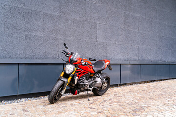 Sporty racing powerful stylish modern red motorcycle stands parked on the road against a dark blue wall with a door. Technology and travel concept