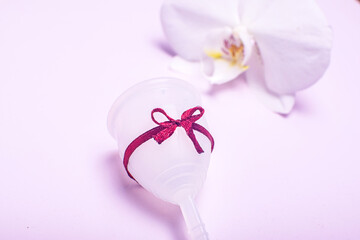 Eco-friendly silicone menstrual cup with orchid on pink background.