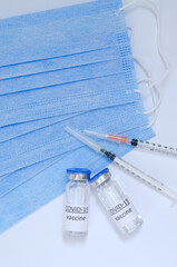 Creative ideas of vaccination concept. Top view of syringe with medical masks and vaccine vial glass bottles for vaccination against COVID-19. Coronavirus pandemic. Copy space. 
