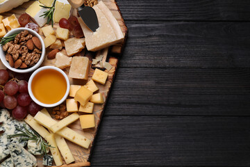 Cheese plate with honey, grapes and nuts on black wooden table, top view. Space for text