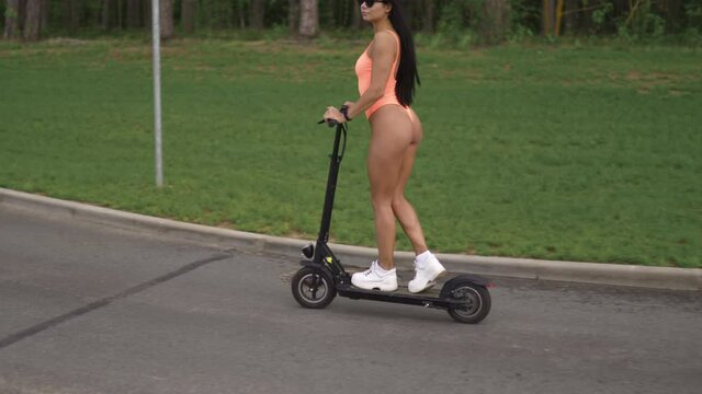 Buttocks view: Young woman riding electric scooter wearing swimsuit