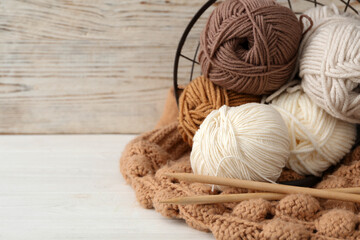 Fototapeta na wymiar Soft woolen yarns with knitting needles and sweater on white table, closeup. Space for text