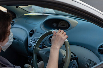 A man in a protective mask wipes the steering wheel with an antibacterial cloth. Infection control concept. Prevent Coronavirus, COVID-19, flu. A man wearing in medical protective mask driving a car.