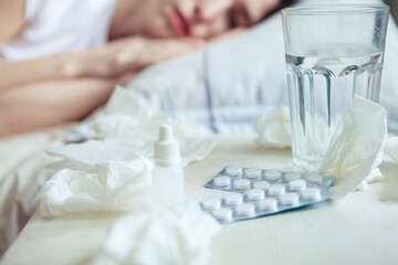 Close-up shot of medicines. In front of the patient's bed are used handkerchiefs, pills, nose drops. The concept of treating colds.