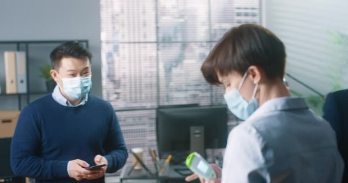 Office workers measure their temperature with electronic thermometer keeping social distance. Concept of new rules and regulations during pandemic.