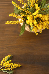 Beautiful mimosa flowers in wicker basket on wooden table, flat lay. Space for text