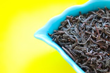 Loose tea leaves in a beautiful bowl with bright yellow background. Dry black tea.