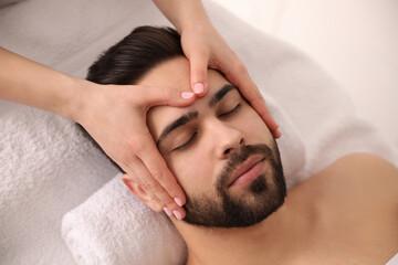 Fototapeta na wymiar Young man receiving facial massage in beauty salon, above view