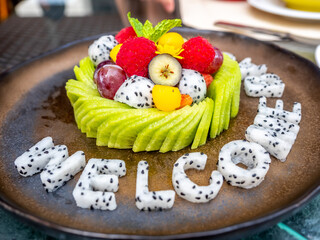 Mixed fruit, watermelon, melon, avocado, kiwi, strawberry, blueberry, dragon fruit, raspberry, decorated on dish with carving 'Welcome Back' 