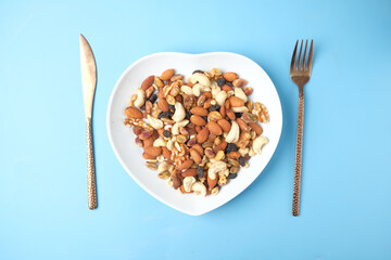 many mixed nuts in heart shape plate on blue background 