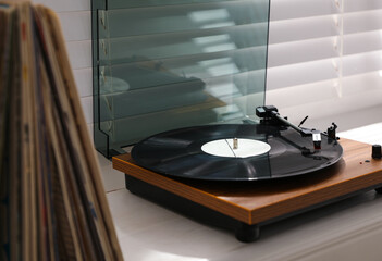 Stylish turntable with vinyl disc on windowsill in room