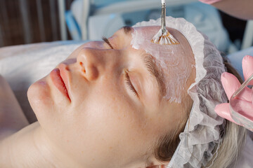 Professional beautician woman applies mask with brush to client's face.