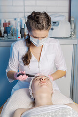 A professional cosmetologist performs an ultrasonic face cleaning procedure for a woman.