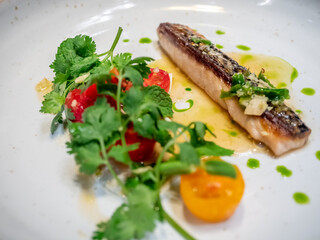 Pan fried mackerel fish with spicy dressing and tomato decorated on white dish in restaurant, selective focus