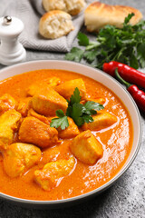 Bowl of delicious chicken curry on grey table, closeup