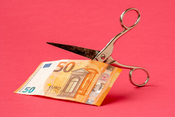 Cutting fifty Euro with scissors on pink background