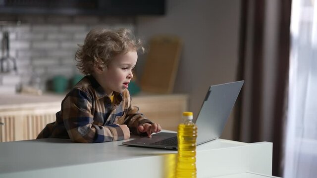 child boy with laptop on kitchen, toddler is using internet for entertainment and education, medium portrait