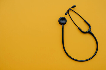 Black medical stethoscope on orange background. Medicine and healthcare concept. Space for text. Flat-lay, top view.