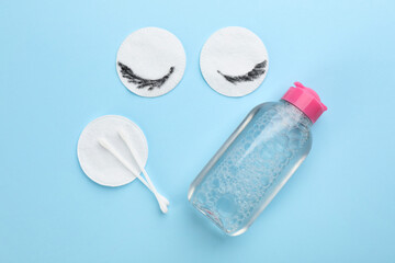 Dirty cotton pads, swabs and micellar cleansing water on light blue background, flat lay
