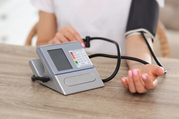 Woman checking blood pressure at wooden table indoors, closeup