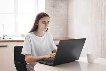 Young woman working on laptop at kitchen. Female freelancer working online
