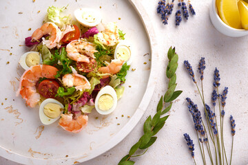 Vegetable salad with quail egg and shrimps, seasoned with oil, on a white plate