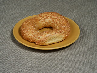 Fresh sesame bagel on a yellow plate on a gray tablecloth