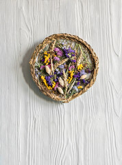 Handmade panel of dried flowers, flowers, wheat, grass and braids hanging on the wall. On a light wooden background