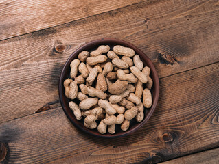 Freshly roasted peanuts on a clay plate on a wooden tabletop