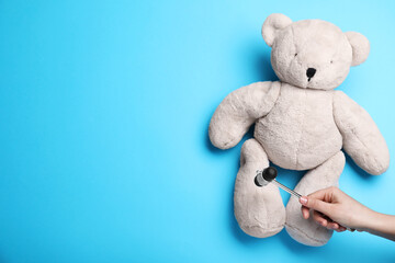 Woman pretending to test teddy bear's reflexes with hammer on light blue background, closeup and space for text. Nervous system diagnostic