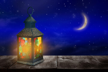 Beautiful decorative Arabic lantern on wooden table at night, space for text. Fanous as Ramadan symbol