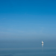 lonely sailing vessel on blue water of vast empty lake under blue sky