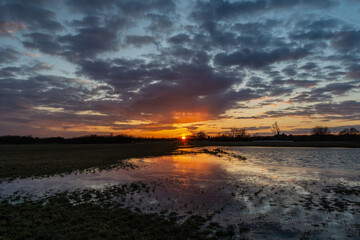 Naklejka premium Sunset and dark clouds on the sky over a meadow with water