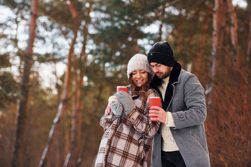 With drink. Cheerful couple have a walk in the winter forest at daytime