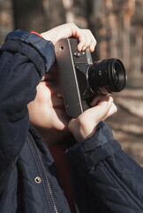 Fototapeta premium A little boy in a blue jacket takes pictures of nature. He has an old vintage camera in his hands
