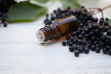 elderberry essential oil jar with freah elderberry berries on wooden background